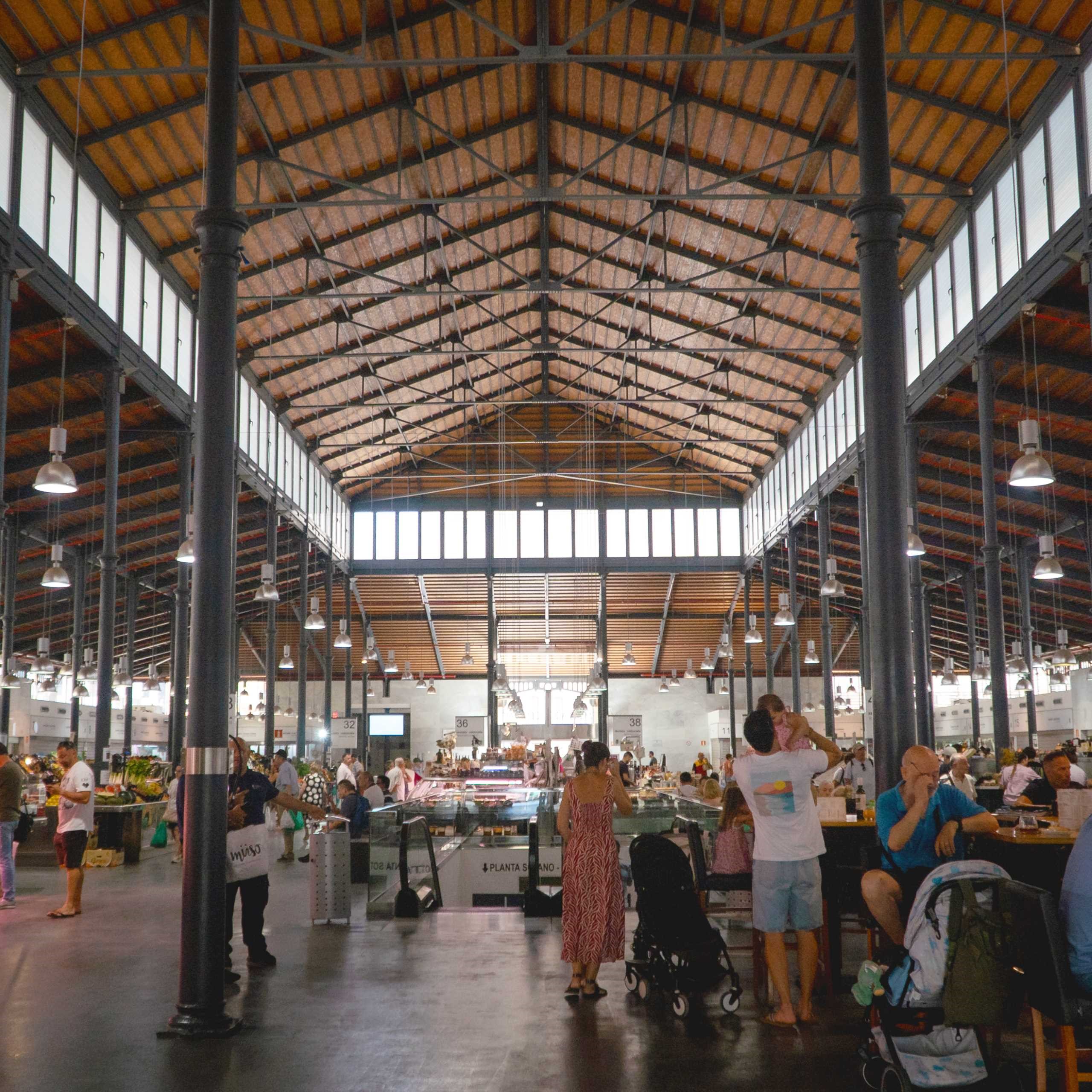 Vista del interior del Mercado Central de Almería con su estructura de hierro, cubierta de madera y puestos gastronómicos con visitantes