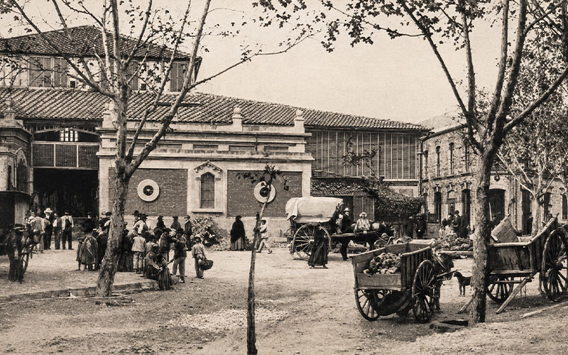 Escena histórica frente al Mercado Central de Almería con vecinos, carros y actividad comercial